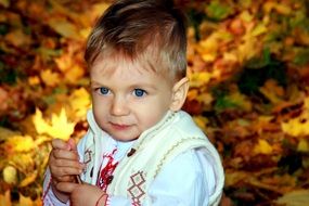 smile of the blue-eyed baby boy standing on a background of yellow autumn leaves