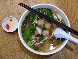 large ball of vietnamese soup with rice noodles, meatballs and greens