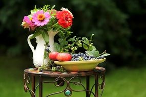 a plate of fruit and a vase of beautiful flowers are on a small table