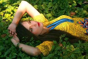 Girl with open eyes in a yellow dress lays on grass