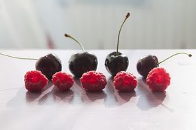 four cherries and five raspberries on a white table