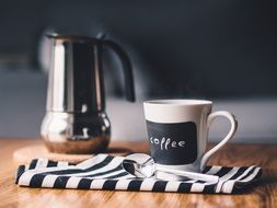 coffee pot with a mug on a striped cloth napkin