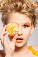 model with orange makeup holding peeled orange