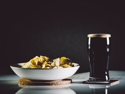 big glass of black beer with a bowl of tacco chips