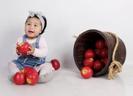 happy little girl is sitting next to a bucket of apples