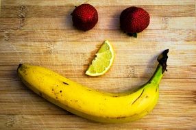 banana, two strawberries and a slice of lemon on a wooden surface