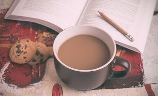cup of coffee with milk, cookies and an open textbook with the pencil on the table