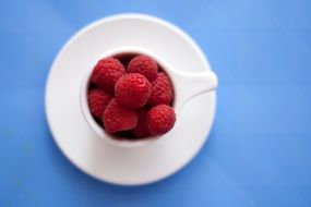 raspberries in a white cup on a blue table
