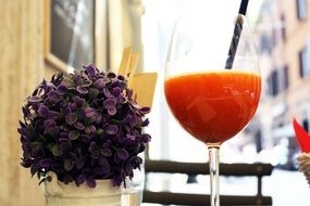 a glass of fresh juice and a potted flower on a table in a cafe