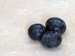 three big blueberries on a white surface