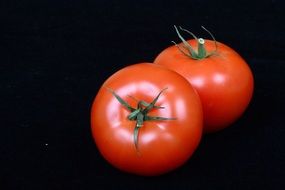 two red ripe tomatoes on a black background