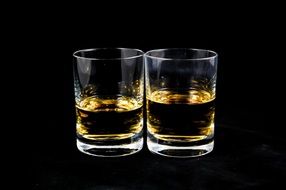 two glasses of whiskey on a black background