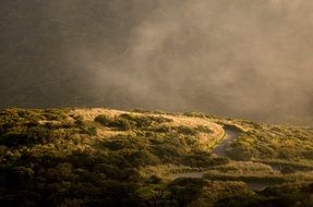 winding road on hillside under stormy clouds