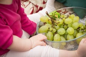 child holding a bowl of green grapes