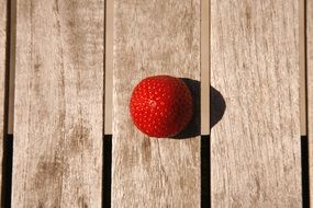 one ripe strawberry on wooden surface