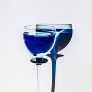 blue glass with drink and its shadow on the white wall