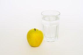 yellow apple and a glass of water on a white background