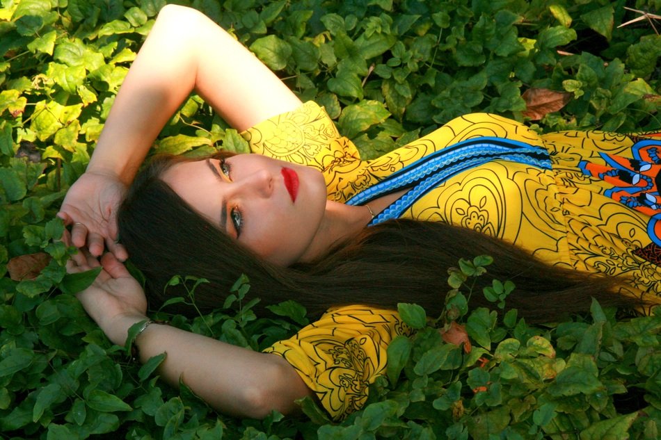 Girl with open eyes in a yellow dress lays on grass