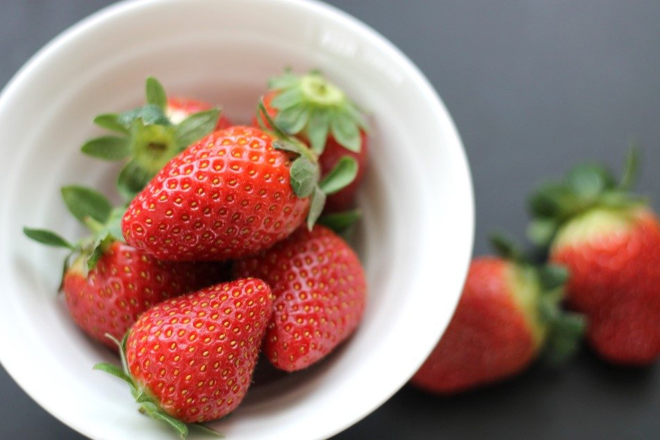 fresh ripe strawberries in white bowl and on the surface