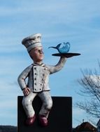 cook with fish on tray, vintage figurine outdoor, restaurant street sign