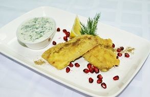 fried fish with pomegranate on a white plate