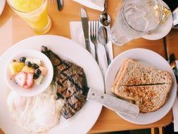 steak with a side dish, toast and a glass of juice on a table in a cafe