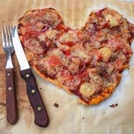 knives lie near a pizza in a heart shape