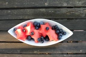 white bowl with berries on wooden planks, top view