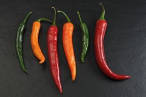 chili peppers of different colors on a dark surface