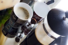 cups and coffee pot with aroma coffee on a mirror surface