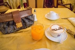 louis vuitton bag, cappuccino cup and fruit drink on the table