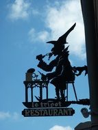 man eating at table on pan, vintage street sign of restaurant at wall, france