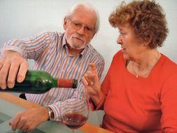 elderly couple is drinking red wine