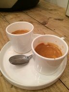 two cups of coffee on a plate in a restaurant