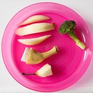 half a banana, half an apple, half pear and broccoli on a plate