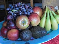 bowl of healthy fresh fruits banana apples plums avocado grape