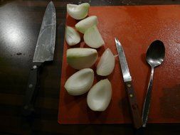 Onion on the chopping board,knives and spoon