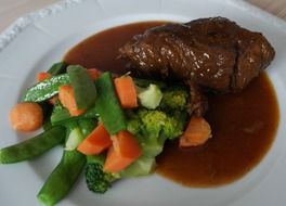 beef roulades with carrots and green vegetables with sauce on a white plate