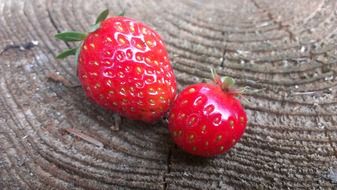 Two red strawberries on a wooden surface