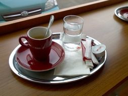 coffee in red cup and water in glass on metal plate