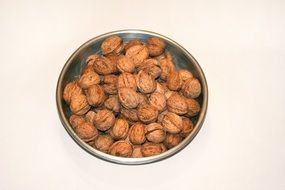 Walnuts in their shells in a bowl on the white surface