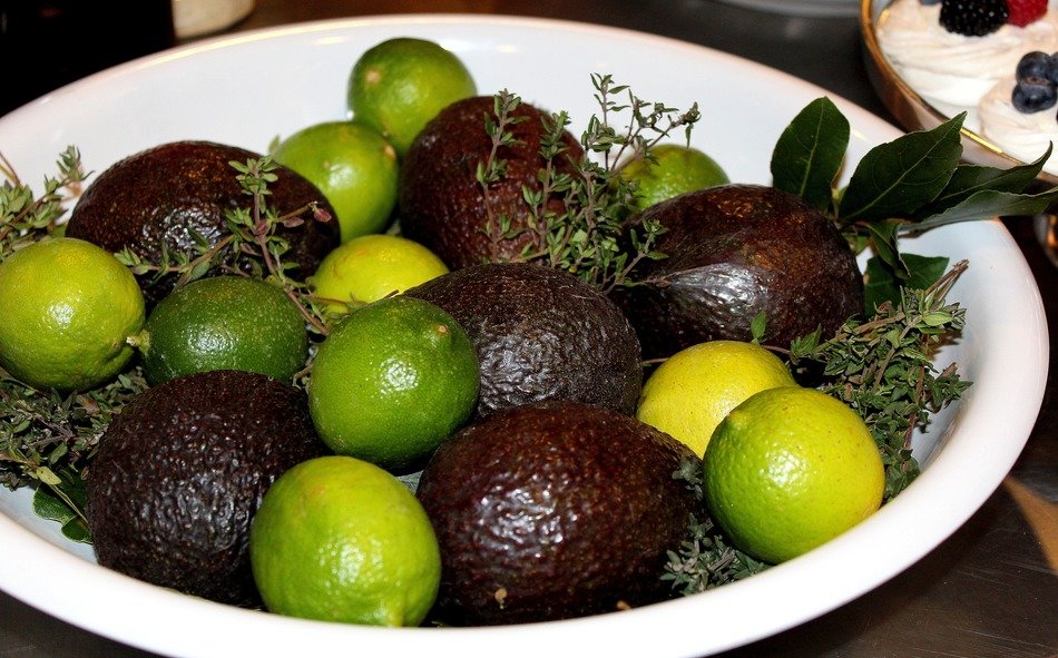 Green limes and black avocadoes in the white bowl