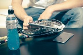 A tennis racket, a bottle of drink and a mobile phone on the table