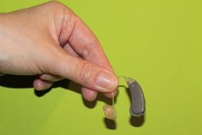 in hand a hearing aid on a light green background