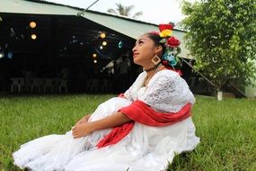 mexican girl in white dress sitting on the green grass