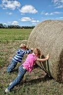 children roll a hay bale across the field