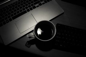 Black and white photo of office desk with laptop and cup of coffee
