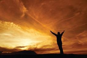 male silhouette with wide open arms at sunset sky