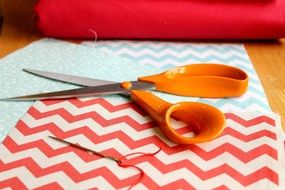 orange scissors and a needle on a striped fabric