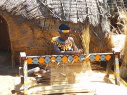 young tribe woman weaving cane at traditional hut, south africa